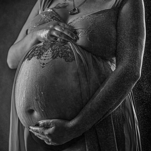 Frau hält ihren nackten Babybauch, während Wasser an ihm herabläuft