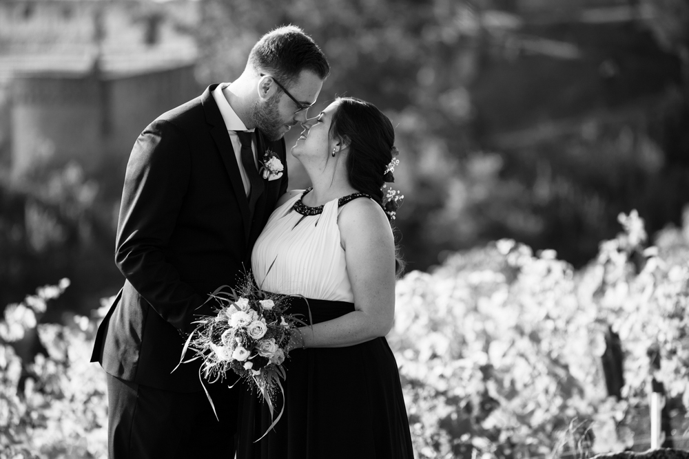 Ein Brautpaar steht eng umschlungen in den Weinbergen der Pfalz. Der Bräutigam küsst zärtlich die Stirn seiner Braut.