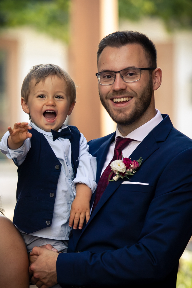 Ein Mann im Anzug hält seinen kleinen Sohn lachend im Arm, beide strahlen in die Kamera. Aufnahme in Wachenheim.