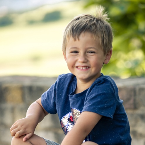Junge sitzt auf einer Mauer und strahlt frech in die Kamera
