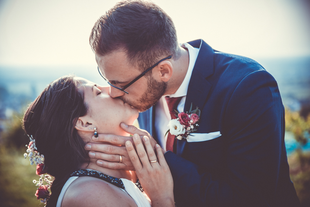 Ein Hochzeitspaar küsst sich liebevoll im Freien, während der Bräutigam das Gesicht der Braut sanft in den Händen hält.