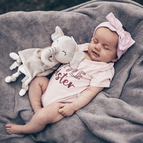 Neugeborenes schläft auf einer weichen Decke mit einem Kuscheltierelefanten in der Hand