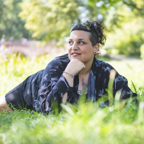 Portrait einer Frau, die auf einer Wiese liegt und verträumt in die Natur schaut